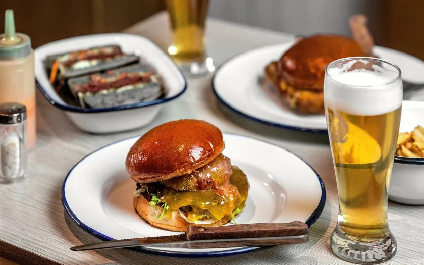 Bữa brunch giản dị với điểm nhấn là chiếc bánh burger lớn và đầy đặn, kèm theo ly bia vàng óng