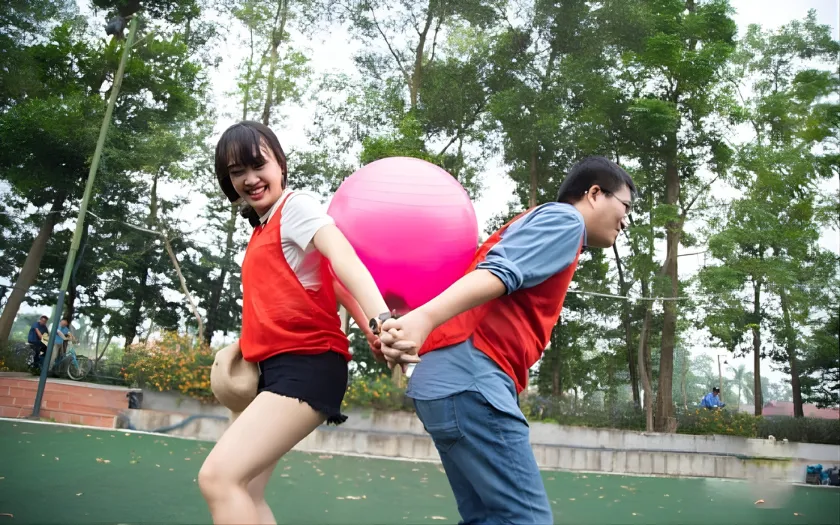 Hai người kẹp bóng bay sau lưng, nắm tay nhau di chuyển trong trò bong bóng vui vẻ