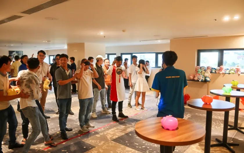 Nhân viên công ty tham gia trò chơi tiệc tất niên trong nhà với người quản trò hướng dẫn.